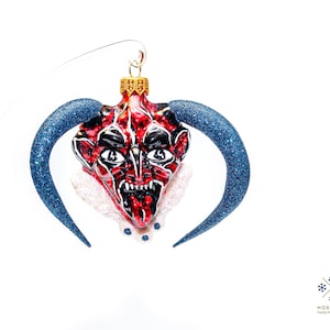 Puede incluir: Adorno de Navidad de vidrio rojo y negro con forma de cabeza de diablo con cuernos de purpurina azul.