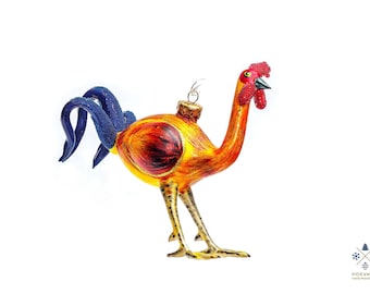 Puede incluir: Adorno navideño de cristal con forma de gallo. El gallo tiene cresta y barbilla rojas, cuerpo amarillo y naranja y cola azul. Está decorado con detalles dorados y tiene un lazo dorado para colgar.