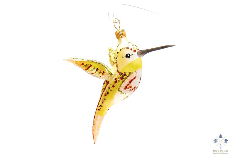 Puede incluir: Un adorno de vidrio amarillo en forma de colibr&iacute; con detalles rojos y verdes. El adorno tiene una barriga blanca y un pico negro.