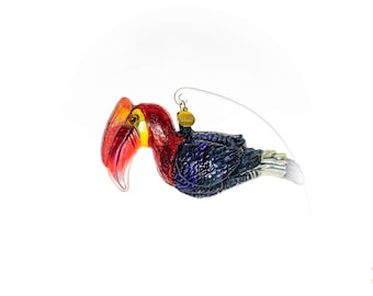 Puede incluir: Un adorno de Navidad de vidrio con forma de pájaro rojo, amarillo y azul con un pico grande. El adorno tiene un colgador dorado.