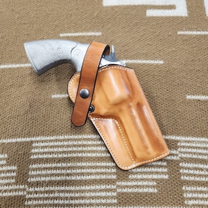 May include: A brown leather holster with a silver revolver inside. The holster has a belt loop and a snap closure.
