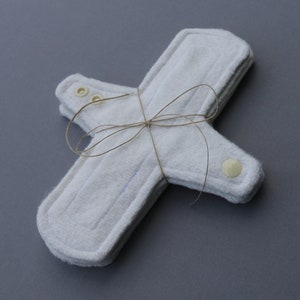 May include: A set of three white reusable cloth menstrual pads with snaps, tied together with twine.