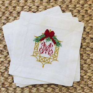 May include: Set of four white linen napkins with a gold embroidered monogram and a red bow with green pine sprigs.