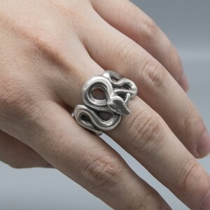 K&ouml;nnte beinhalten: Ein silberner Schlangenring mit einem detaillierten Design. Die Schlange ist zusammengerollt und ihr Kopf ist erhoben.