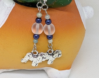 Puede incluir: Pendientes de plata con un racimo de tres elefantes de plata colgando de una cadena. La cadena está unida a una cadena de cuentas, incluyendo cuentas de color rosa claro, azul y blanco.
