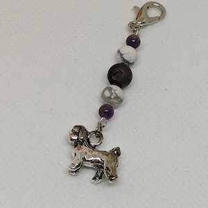 Puede incluir: Un brazalete con un dije de plata de un perro, una piedra negra y blanca y una piedra morada, con un cierre de plata.