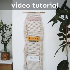 以下が含まれることがあります： 3つのポケットが付いた白いマクラメの壁掛け。ポケットには、「ステートメントマクラメ」、「レイン」、「ニュースクールマクラメ」というタイトルの雑誌が入っています。