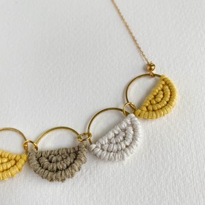 May include: A gold chain necklace with four crocheted half-circle pendants in yellow, white, and brown.