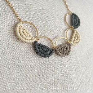 May include: A gold chain necklace with five half-circle pendants made of macrame in beige, grey, and brown.