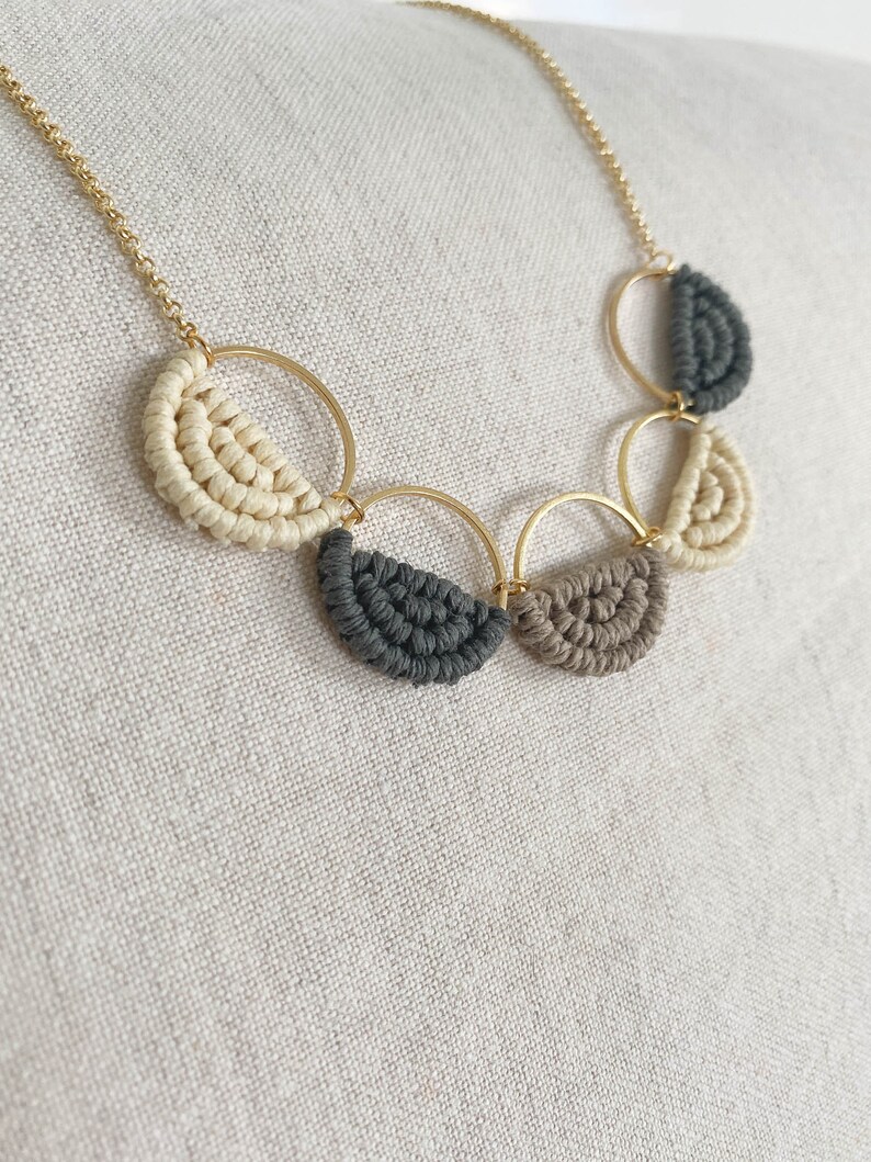 May include: A gold chain necklace with five half-circle pendants made of macrame in beige, grey, and brown.