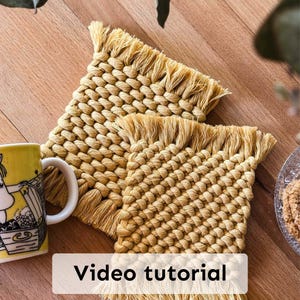 Könnte beinhalten: Zwei quadratische, gewebte, beige Untersetzer mit Fransen. Links ist ein gelber Becher mit weißem Henkel und einer Cartoon-Illustration. Der Text "Video tutorial" wird unten im Bild angezeigt.