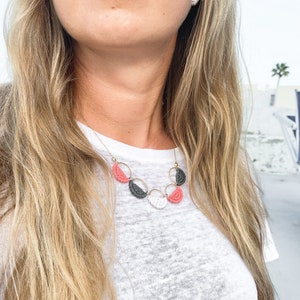 May include: A gold necklace with a layered design of pink, white and grey half-circle beads.