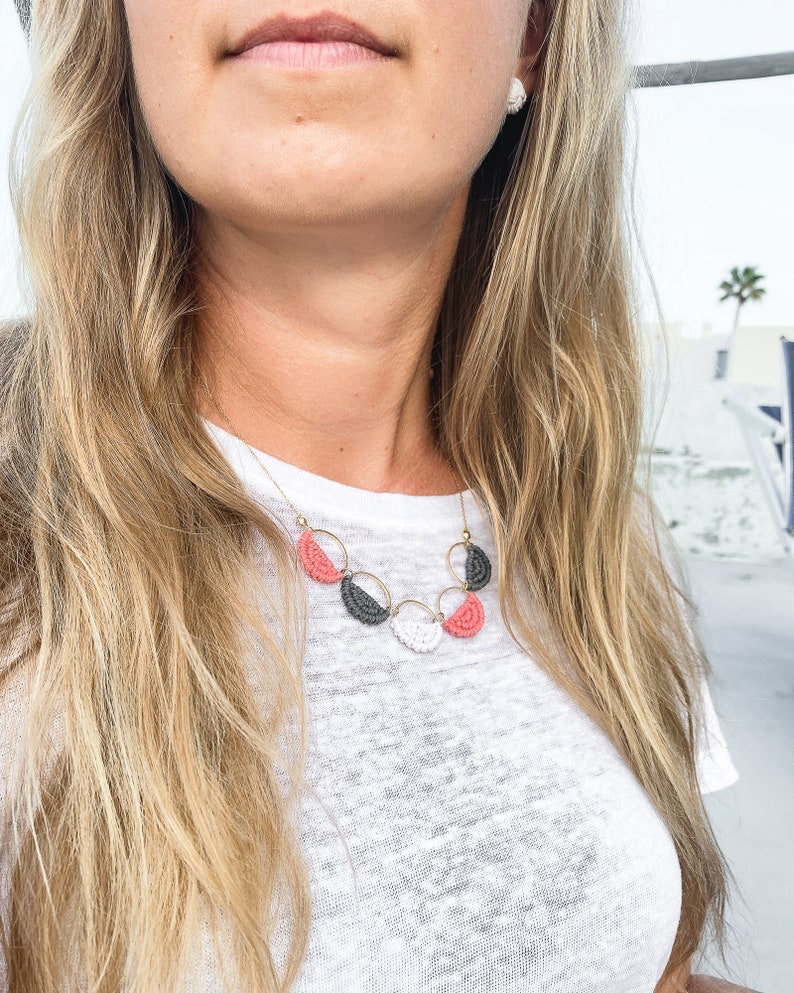 May include: A gold necklace with a layered design of pink, white and grey half-circle beads.