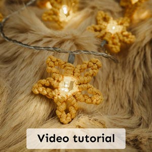 May include: A string of star-shaped lights, made from a light tan material, glows against a soft, textured backdrop. The lights are linked by a silver wire. The text "Video tutorial" is displayed on a white rectangle.