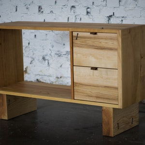 Puede incluir: Una consola de madera clara con dos cajones y un estante abierto. La consola tiene un diseño simple y moderno y está hecha de madera maciza.