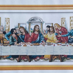 May include: A framed cross-stitch of the Last Supper. The image shows Jesus and his disciples at a table, with detailed stitching in various colours. The frame is gold-coloured.