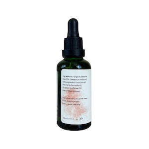 May include: A green glass bottle with a black dropper top. The bottle contains a clear liquid and has a white label with the text "Ingredients: Organic Sesame Seed Oil (Sesamum Indicum). Ashwagandha Root Extract (Withania Somnifera). Organic Sunflower Oil (Helianthus Annuus) Store in a cool, dry place away from direct sunlight. For external use only 50ml/1.7 fl. oz e"