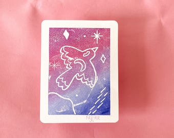 Könnte beinhalten: Eine rechteckige Karte mit weißem Rand zeigt ein stilisiertes Vogeldesign in Weiß vor einem Farbverlauf aus Rosa, Lila und Blau. Das Design umfasst Sterne und Rauteformen. Die Initialen des Künstlers, "NRJRR", befinden sich in der unteren rechten Ecke.