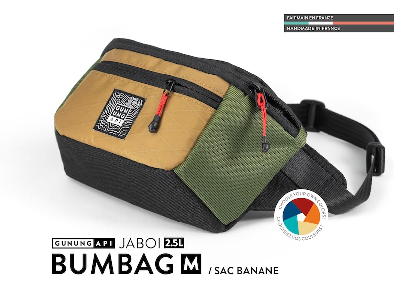 May include: A multi-colored bum bag with the text "GUNUNG API JABOI 2.5L BUMBAG M / SAC BANANE". The bag features a black base, a tan front panel, and an olive green side panel. It has red zipper pulls and a black adjustable strap.