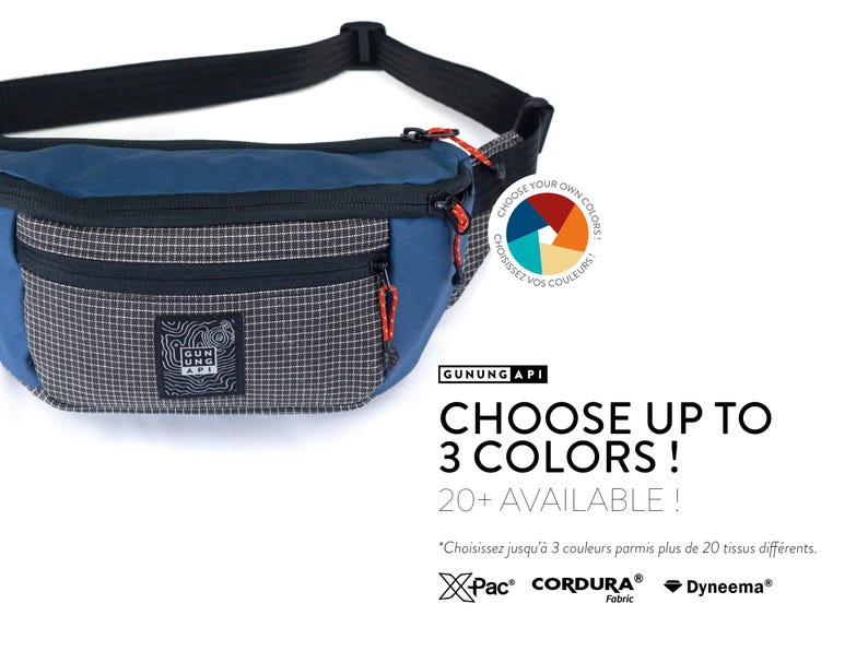 May include: Blue and gray fanny pack with a black strap and red zipper pulls. The pack has a checkered pattern on the front pocket and the text "GUNUNG API". The text "CHOOSE UP TO 3 COLORS!" is also visible.