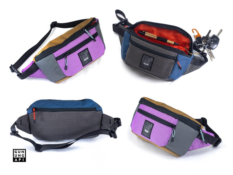 May include: A collection of colorful fanny packs in various angles. The bags feature a mix of colors including purple, blue, brown, and gray. Each bag has a black adjustable strap and a zippered compartment. One bag is open, revealing an orange interior and a pen.