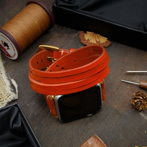 May include: A bright orange leather watch band wraps around a silver smartwatch. The band is made of three separate straps that are stitched together. The watch band is on a wooden surface.