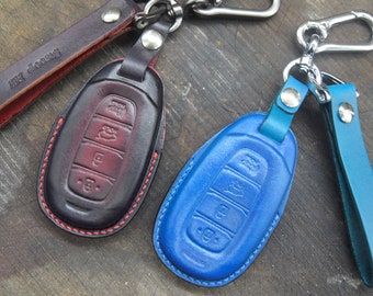 May include: Two leather keychains with key fobs. One keychain is black with red stitching and the other is blue with white stitching. Both keychains have a silver metal hook.