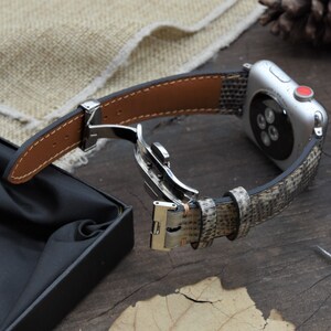 May include: A brown leather watch band with a snakeskin pattern and a silver buckle. The band is attached to a silver Apple Watch.