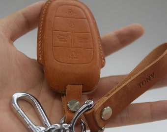 May include: A brown leather key fob with a silver key ring and a brown leather strap with the word "TONY" embossed on it. The key fob has four buttons with the word "HOLD" printed on each button.