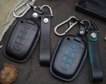 May include: Two leather keychains with car key covers. One keychain is black with the word "OLIVE" on the strap. The other keychain is blue and green with the word "TIMIKE" on the strap.