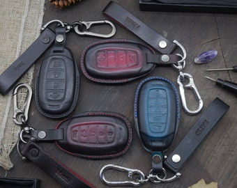 May include: Four leather key covers with different colored stitching and a metal key ring. The key covers are black, red, blue, and brown. The key ring has a silver metal clasp. The key covers have the words "Mark", "OLTV", "ROGX", and "MANT" embossed on them.