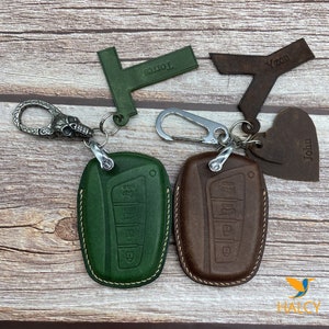Pode incluir: Dois chaveiros de couro com nomes personalizados. Um chaveiro é verde com um amuleto de caveira e o outro é marrom com um amuleto de coração. Ambos os chaveiros têm um clipe de metal e um porta-chaves de couro.