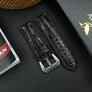 May include: Two black alligator watch straps with a silver buckle. The straps have a textured pattern.