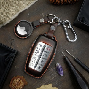 May include: A brown leather key fob with a silver key chain and a silver car key with multiple buttons. The key fob has the word "HOLD" printed on it.