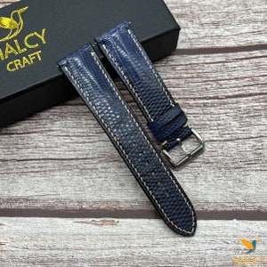 May include: Two dark blue leather watch straps with white stitching. The straps are made of lizard skin and have a silver buckle.