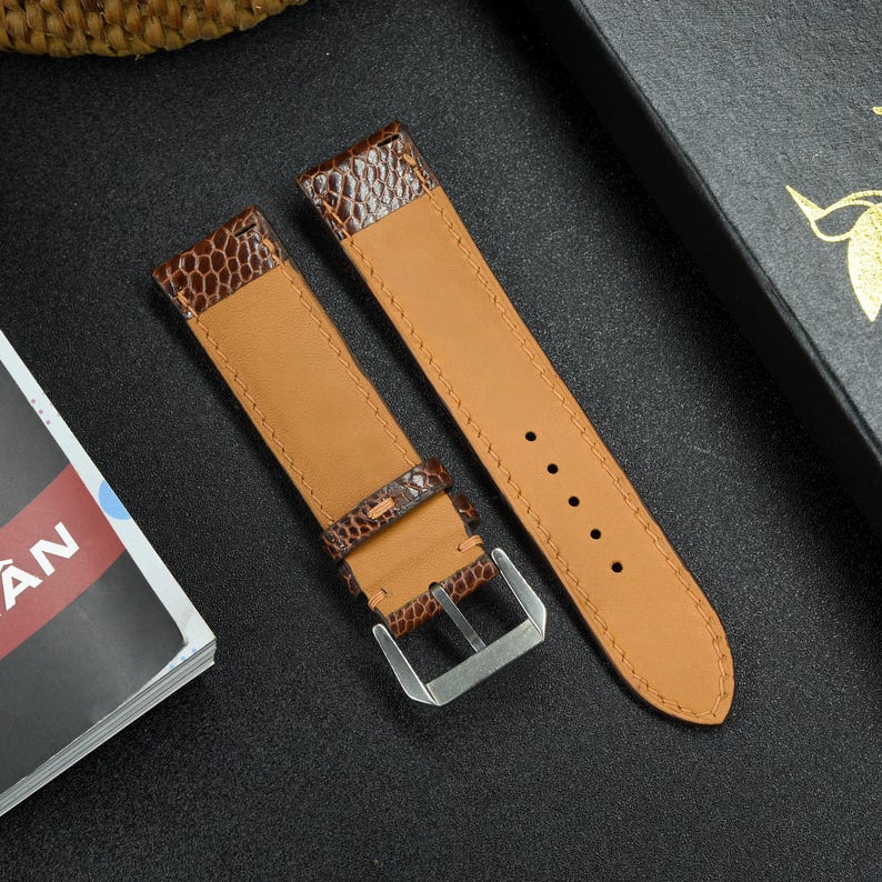 May include: Two brown leather watch straps with stitching detail. One strap has a buckle and the other has a plain end.