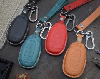 May include: Five leather key covers with metal key rings and clips. The covers are in black, teal, red, and tan.