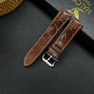 May include: Two brown leather watch straps with a textured ostrich skin pattern. The straps have silver buckles.