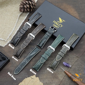 Può includere: Cinque cinturini per orologio in pelle di diversi colori con un sottile motivo testurizzato. I cinturini sono disposti in fila su una superficie di legno. I colori sono nero, marrone, verde scuro, verde e oliva. I cinturini sono etichettati con i loro rispettivi colori. Il nome del marchio "HALCY CRAFT" è visibile su una scatola nera sullo sfondo.