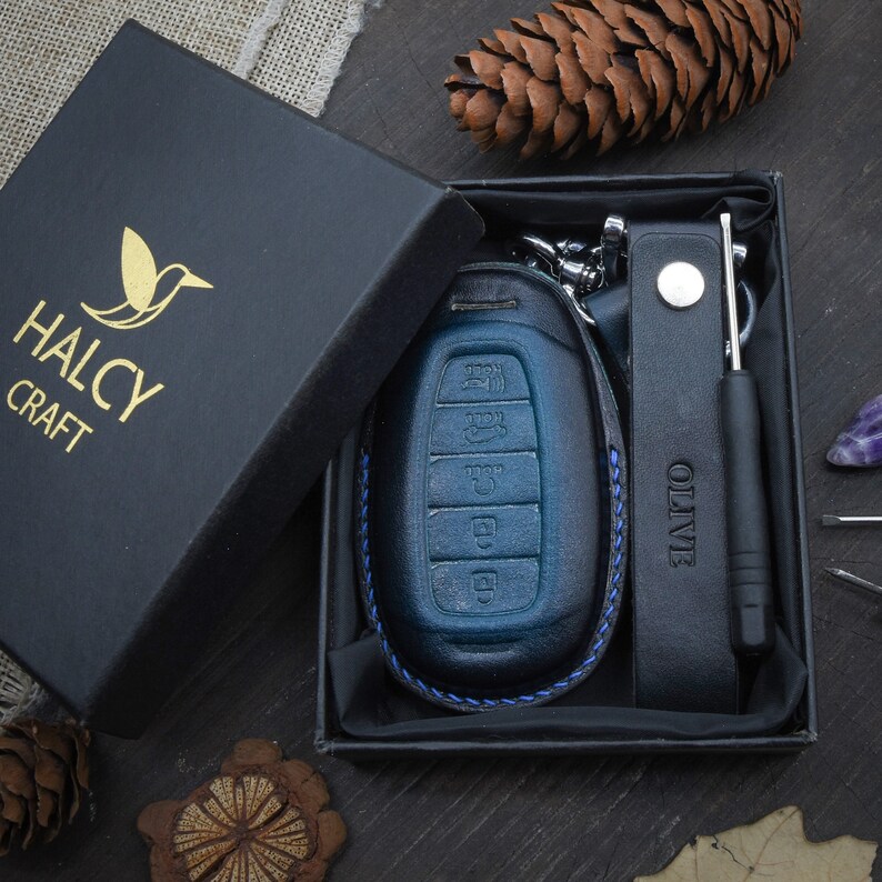 May include: A blue leather key fob with a black leather strap and a small screwdriver. The key fob is in a black box with the logo "HALCY CRAFT" on the lid.