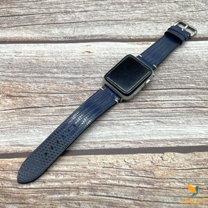 May include: A blue leather watch band with a textured pattern. The band is attached to a silver Apple Watch.