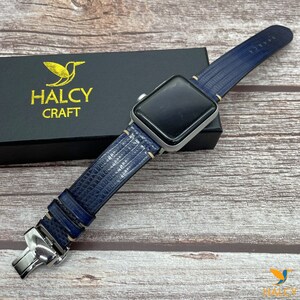 May include: A blue leather watch strap with white stitching and a silver buckle. The strap is attached to a silver Apple Watch.