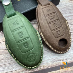 May include: Two leather key covers, one green and one brown, with stitching around the edges. Both covers have multiple buttons and the green cover has the word "NISSAN" embossed on it.