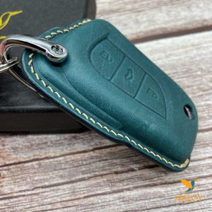 May include: A teal blue leather key fob with a cream coloured stitch detail. The fob has three buttons with the letters "EL", "ED", and a symbol.