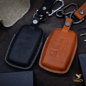 May include: Two leather key covers, one black and one brown, with stitching around the edges. Both covers have a raised design of a car key with buttons.