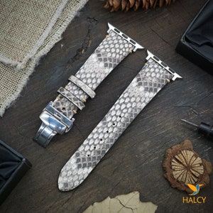 May include: A gray and white snakeskin Apple Watch band with a silver buckle. The band is made of genuine leather and has a classic design.