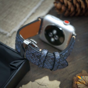 Könnte beinhalten: Ein blaues Lederarmband mit einer silbernen Schließe. Das Armband ist aus echtem Schlangenleder gefertigt und hat ein strukturiertes Muster. Das Armband ist für eine Apple Watch konzipiert.