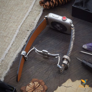 May include: A brown leather Apple Watch band with a snakeskin pattern. The band has a silver buckle and is shown on a wooden surface.