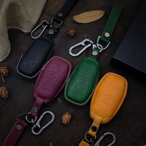 Peut inclure: Quatre porte-clés en cuir avec des housses de clés de différentes couleurs. Les housses de clés sont noires, bordeaux, vertes et jaunes. Chaque porte-clés est doté d'un crochet en métal argenté.