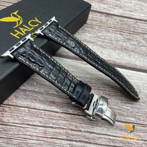 Op de afbeelding: Zwart leren horlogeband met witte stiksels en een roestvrijstalen gesp. Het band is ontworpen voor Apple Watches.